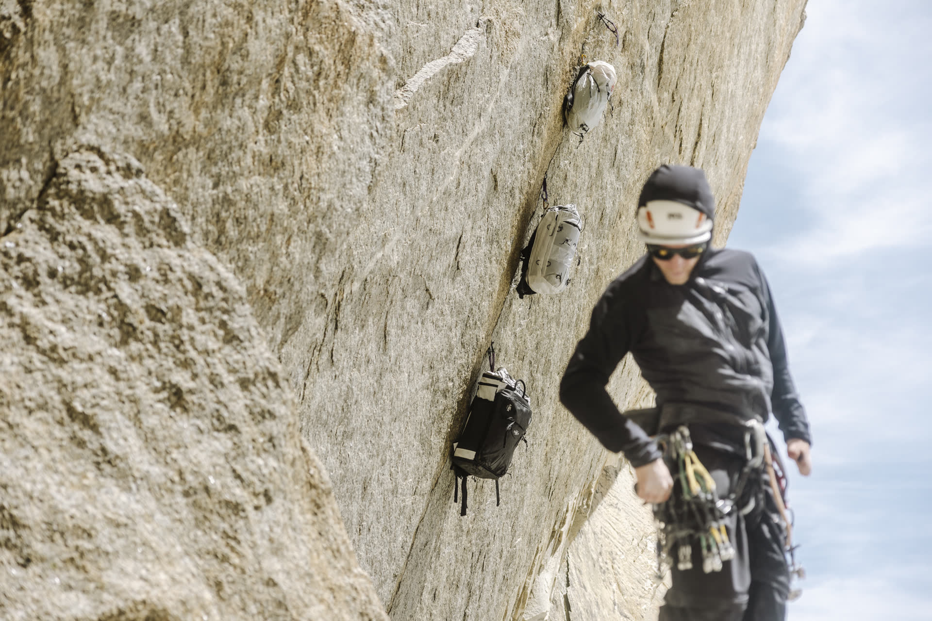 Three packs hanging from a crack, climber at the belay